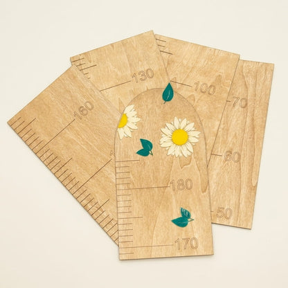 Five wooden height measurement boards with printed growth charts and daisy illustrations, arranged overlapping on a light beige background.