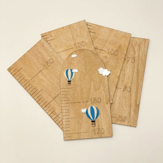 Five wooden arch-shaped growth charts with printed measurement markings and small blue-and-white hot air balloon illustrations, arranged on a light beige background.