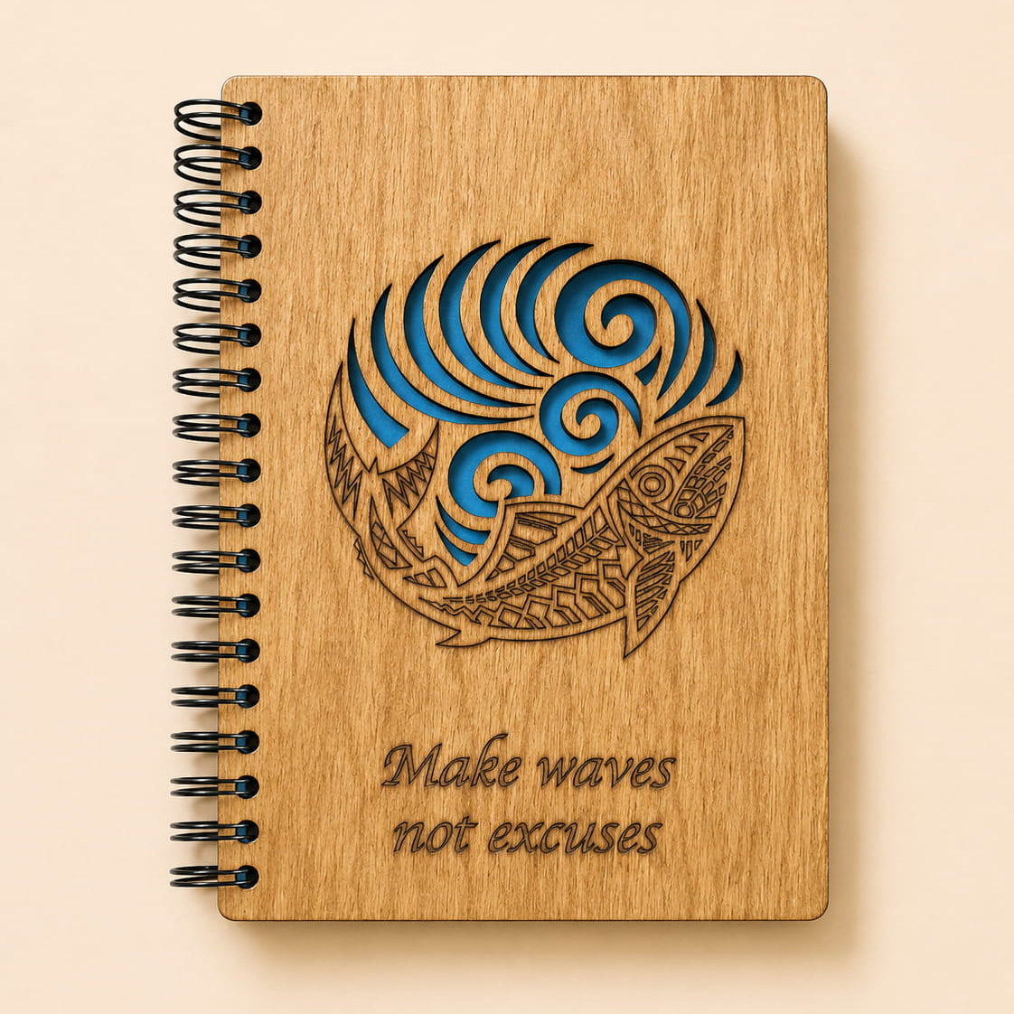 A spiral-bound wooden notebook with a laser-engraved design of a fish and waves, with the text 'Make waves not excuses' on a light beige background.
