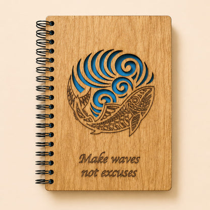 A spiral-bound wooden notebook with a laser-engraved design of a fish and waves, with the text 'Make waves not excuses' on a light beige background.