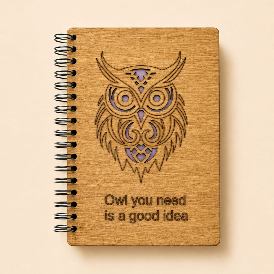 A spiral-bound notebook with a light wood cover featuring a laser-engraved owl design and the text 'Owl you need is a good idea'.