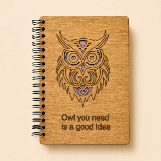 A spiral-bound notebook with a light wood cover featuring a laser-engraved owl design and the text 'Owl you need is a good idea'.