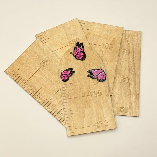 Five wooden height rulers with pink and black butterfly illustrations, arranged on a light beige background.